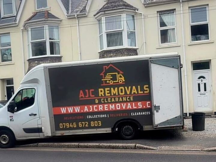 Two branded AJC Removals Luton vans parked outside a terraced house in Cornwall