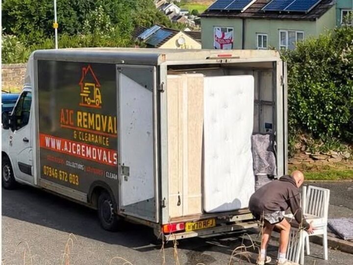 An AJC Removals team member loading a mattress and furniture into the van